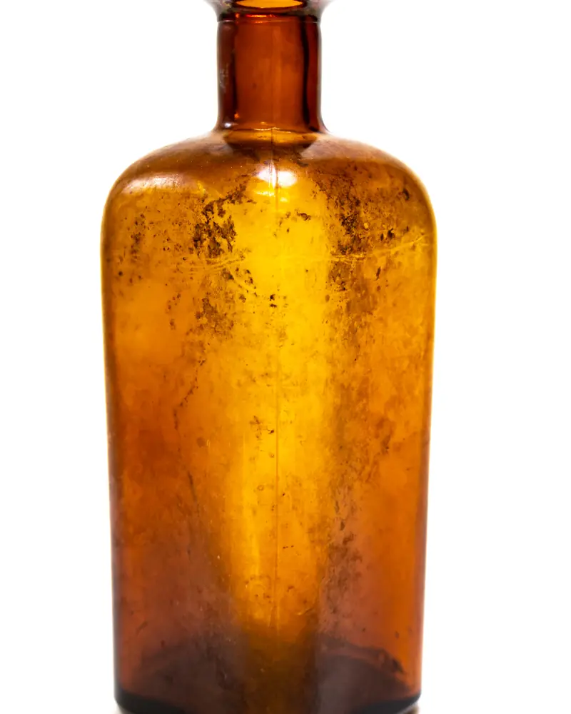 Old square amber glass pharmacy bottle, with no stopper or label, on a white background