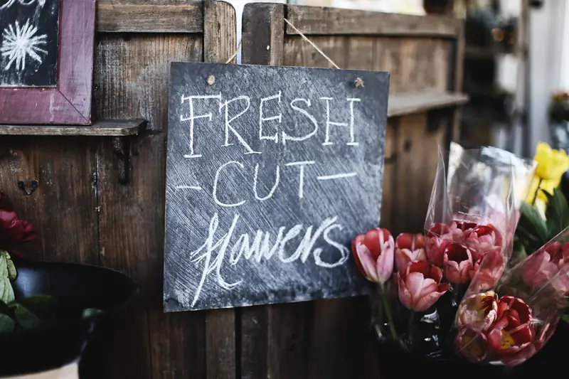Ardoise « Fresh cut flowers » écrite à la craie à côté de bouquets de tulipes emballés