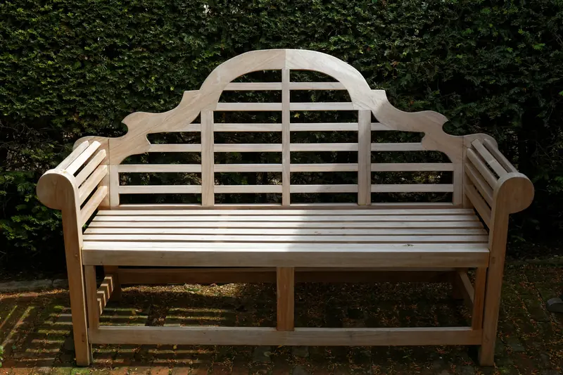 Pale wooden garden bench with a curved back in front of a clipped hedge