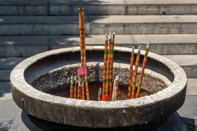 Bâtons d'encens plantés dans un grand brûle-parfum de pierre devant un temple