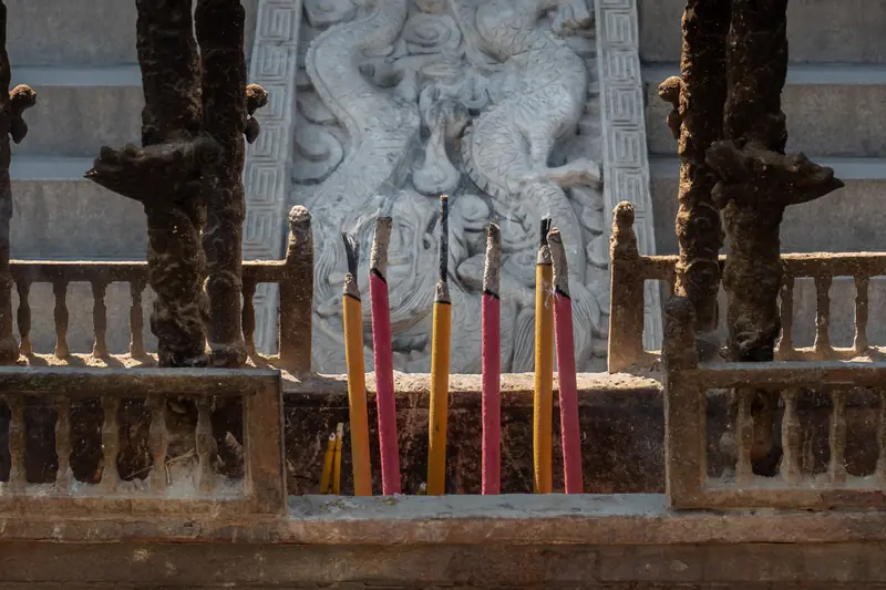 Bâtons d'encens rouges et jaunes plantés devant un mur sculpté d'un temple chinois