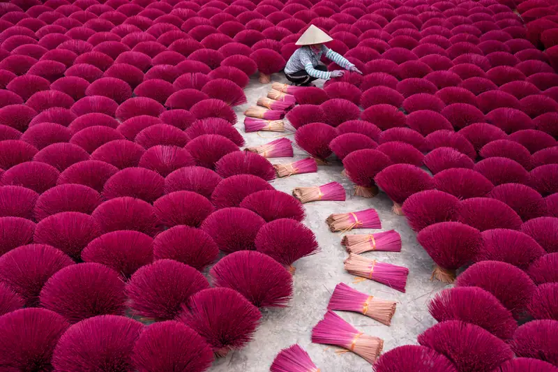 Red incense sticks drying in fans in Vietnam, an artisan in a conical hat in the distance