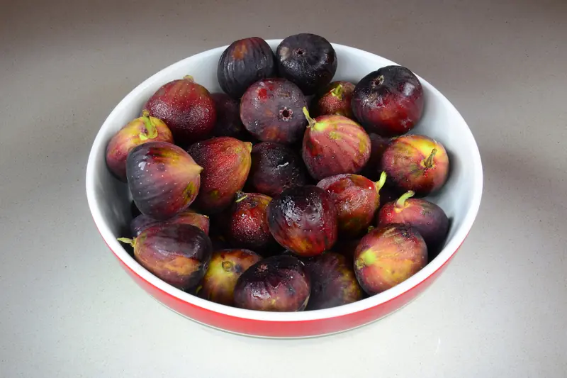Bol rempli de figues violettes mûres posé sur une table claire