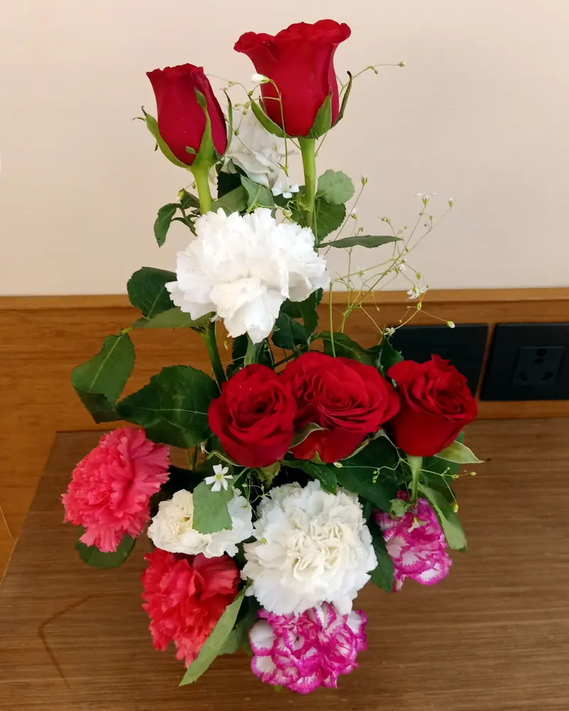 Bouquet de roses rouges, d'œillets roses et d'œillets blancs posé sur une table en bois