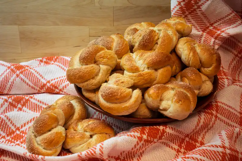 Brioches tressées à la cardamome dans un bol en bois sur une nappe à carreaux rouges
