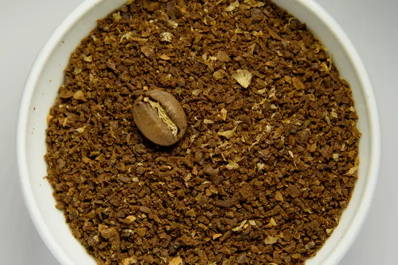 Café moulu grossièrement dans un bol blanc avec un grain entier posé dessus