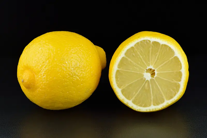 A whole lemon and a halved lemon on a black background, pale yellow flesh and glossy peel