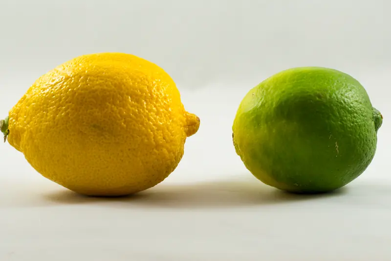 Un citron jaune et un citron vert posés côte à côte sur un fond blanc lumineux