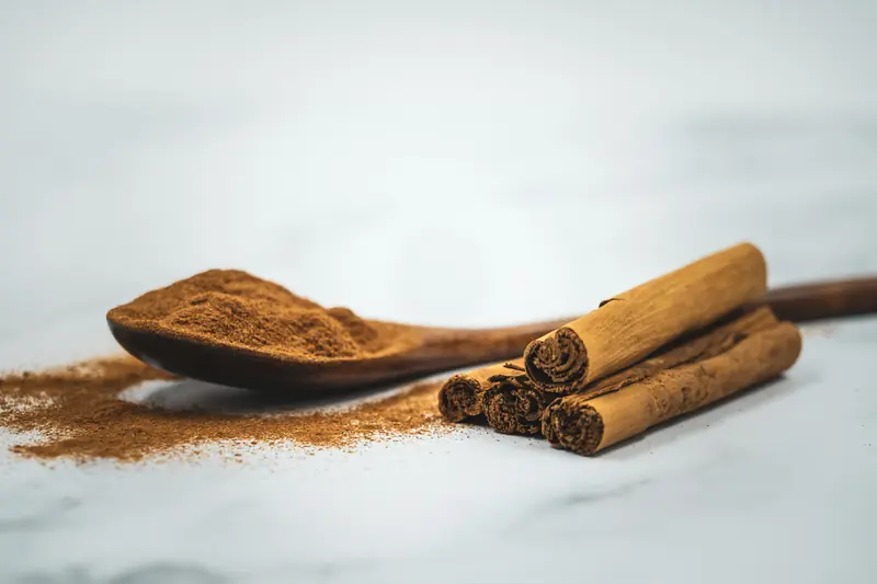 Wooden spoon of ground cinnamon beside cinnamon sticks on marble