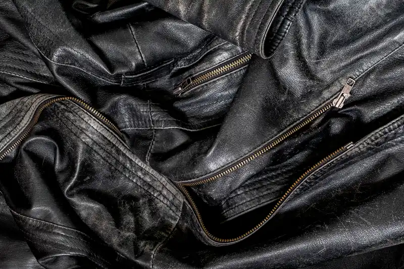 Détail d'un blouson en cuir noir usé, plis brillants et fermeture éclair