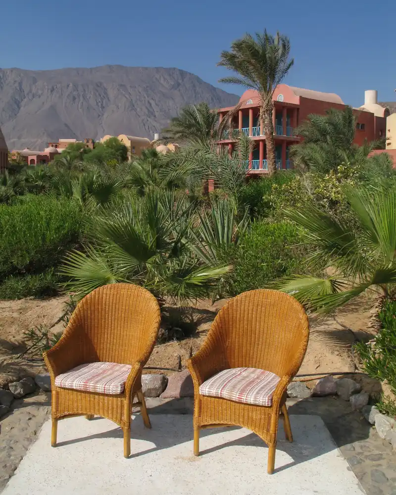 Deux fauteuils en osier face à un jardin de palmiers et de montagnes, dans le Sinaï