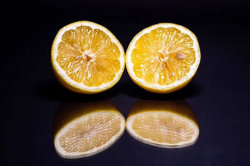 Two lemon halves on a dark glossy surface that mirrors their flesh