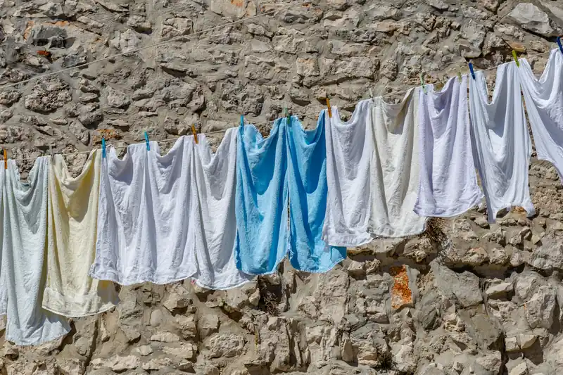 Draps et serviettes pâles alignés sur un fil devant un mur de pierres en Istrie