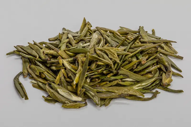 Long, slender dried green tea leaves in a small heap on a light grey background