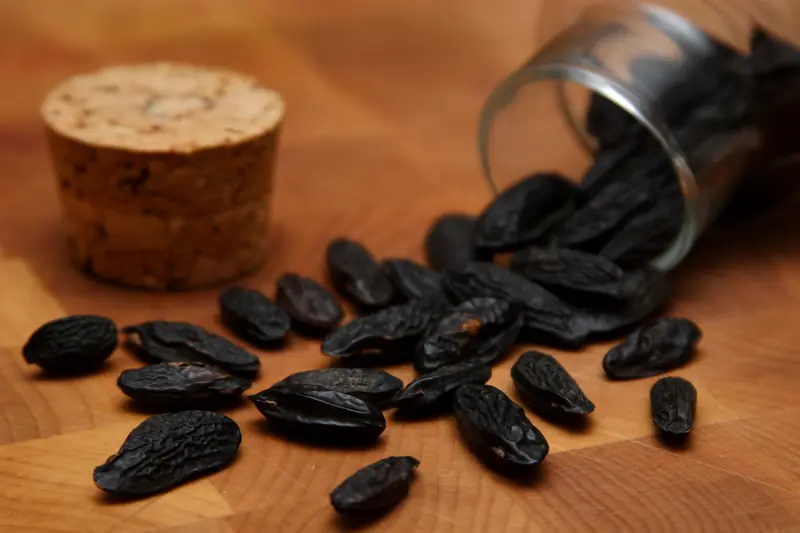 Fèves tonka noires et ridées renversées d'un bocal à bouchon de liège sur une planche