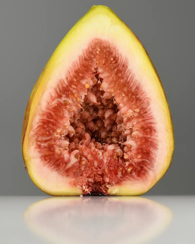 Fig cut in half, red flesh and green skin, on a grey reflective background