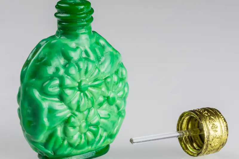 Flacon de parfum ancien en verre vert moulé de fleurs et son bouchon doré à côté