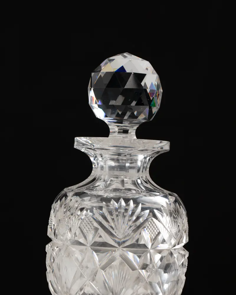 Flacon de parfum en cristal taillé à bouchon facetté, sur fond noir