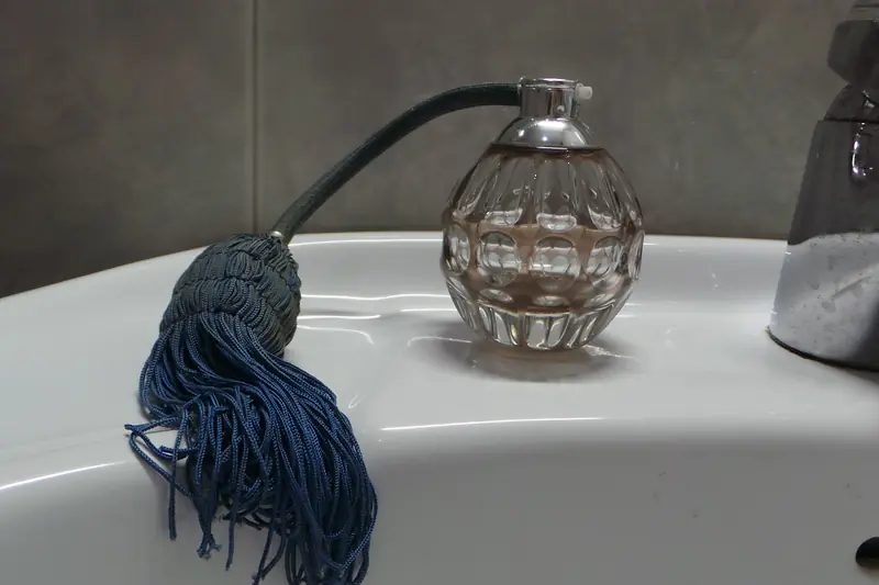 Flacon de parfum en verre ciselé à poire en passementerie bleue posé au bord d'un lavabo