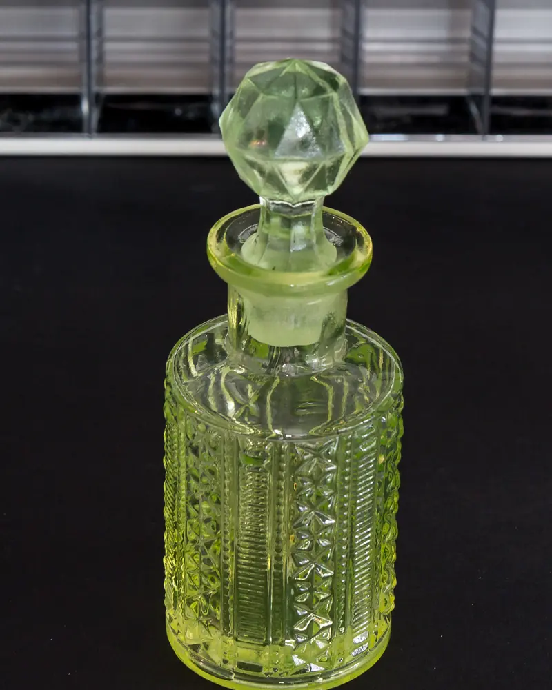 Flacon de parfum en verre jaune-vert ciselé à bouchon taillé sur fond sombre