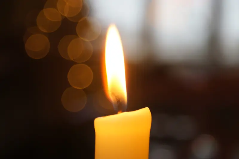 Flamme d'une bougie jaune en gros plan devant des reflets dorés flous