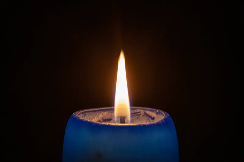 Flamme d'une bougie dans un photophore bleu se détachant sur un fond noir