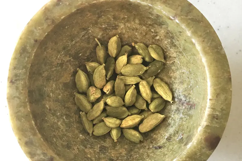 Dried green cardamom pods heaped inside an old, worn brass mortar