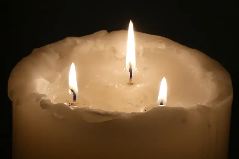 Grosse bougie blanche à trois mèches allumées dans l'obscurité