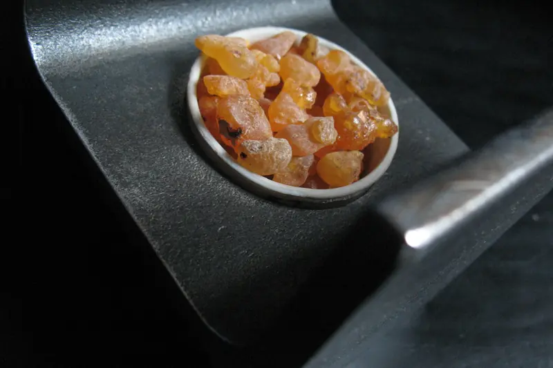 Amber frankincense tears in a small dish on a black metal stand