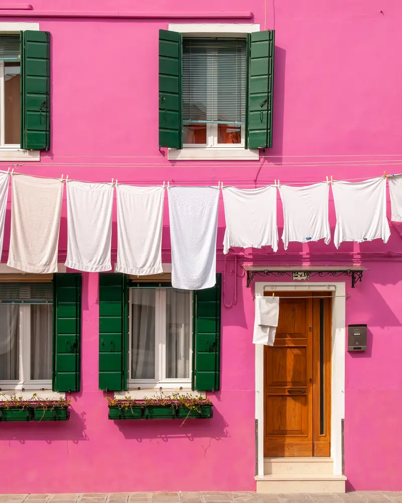 Linge blanc qui sèche sur un fil tendu devant une façade rose vif de Burano
