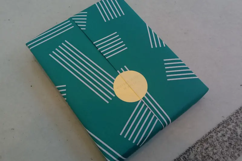 Livre emballé en cadeau dans un papier turquoise à rayures fermé par une pastille dorée