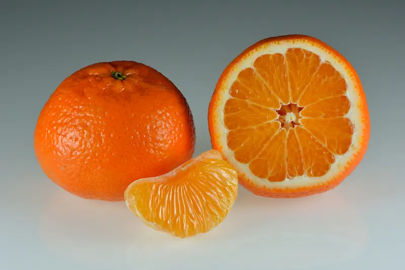 Mandarine entière, mandarine coupée en deux et un quartier épluché sur fond gris