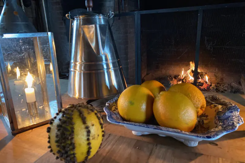 Orange piquée de clous de girofle près d'une coupe d'oranges, devant un feu de cheminée
