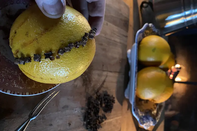 Orange en train d'être piquée de clous de girofle en ligne, sur une table en bois