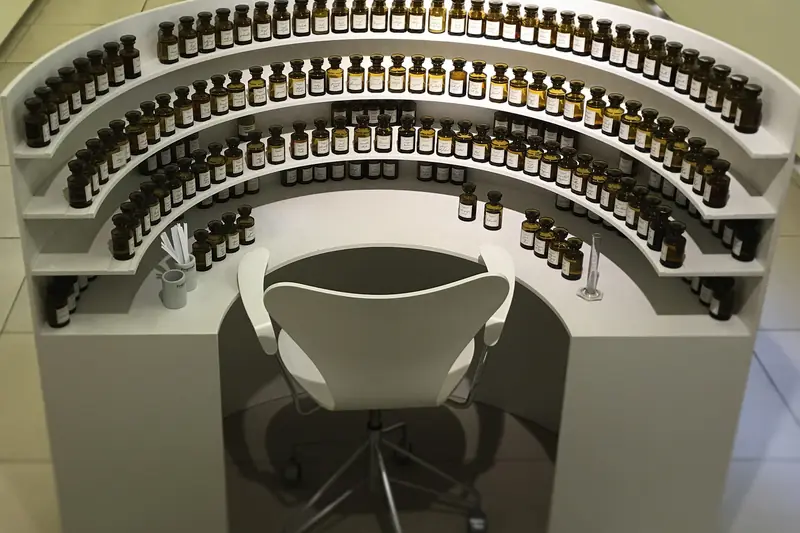 Orgue de parfumeur blanc en hémicycle, flacons bruns en gradins autour d'une chaise
