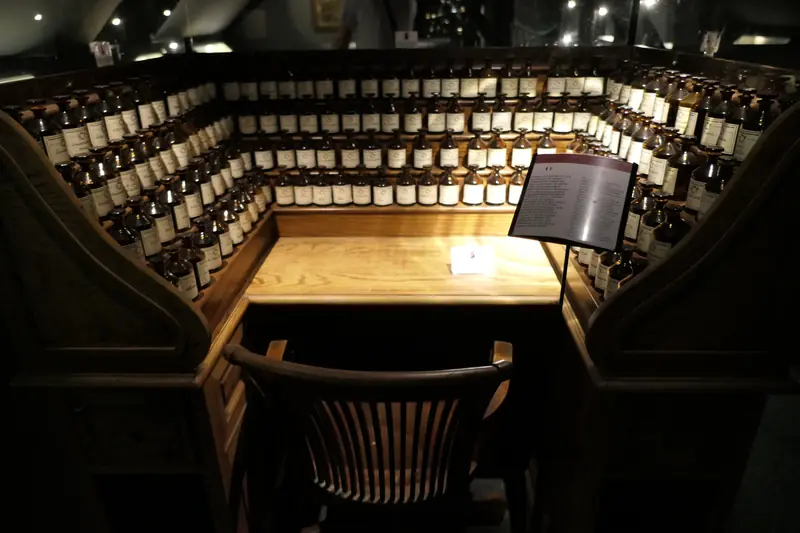 Orgue à parfums ancien en bois sombre, centaines de flacons autour d'un bureau éclairé