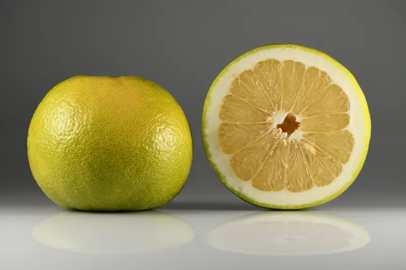 Oroblanco entier et coupé en deux, chair jaune pâle, posé sur un fond gris
