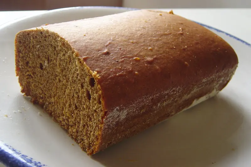 Pain d'épices entamé, mie brune et croûte glacée, sur une assiette blanche