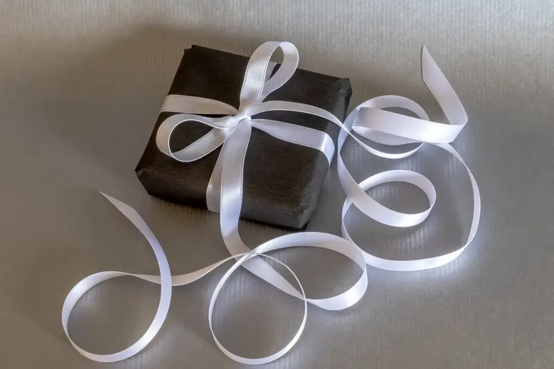 Paquet cadeau gris foncé entouré d'un long ruban de soie blanc en boucles