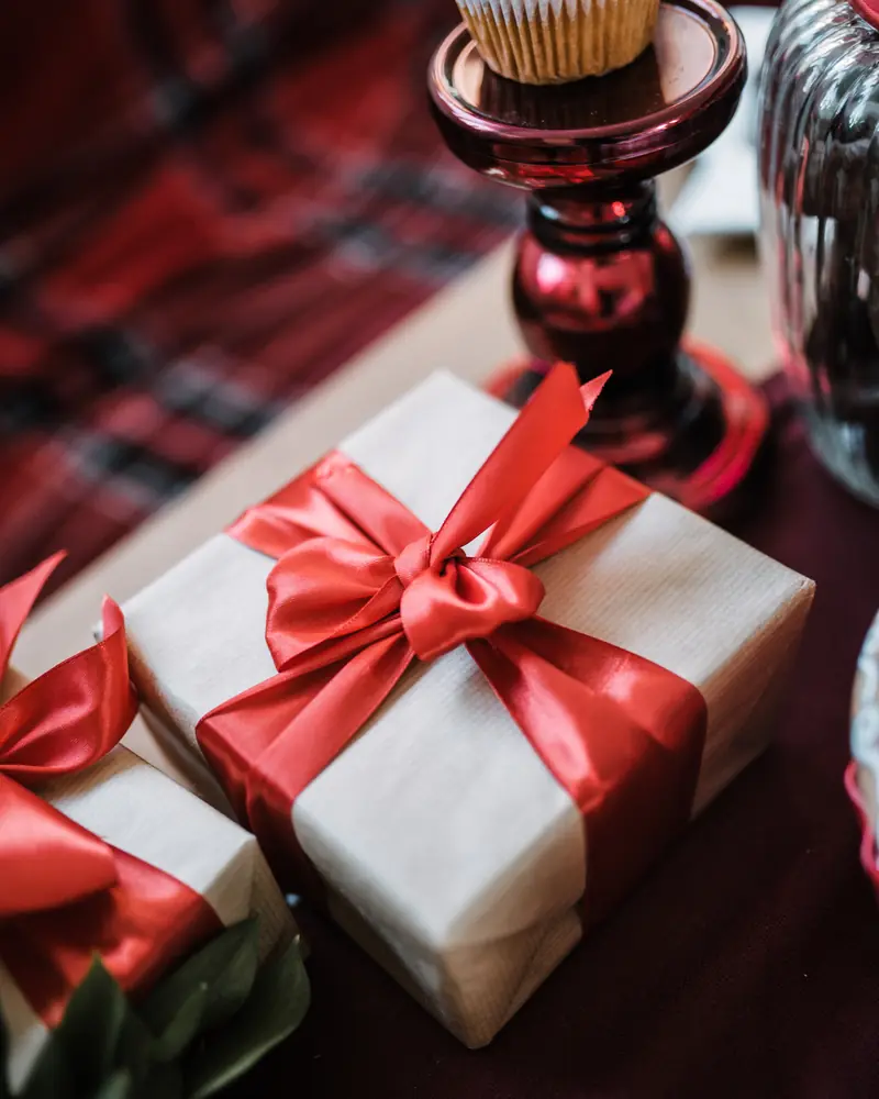Paquet cadeau en papier crème noué d'un ruban rouge sur une table de fête