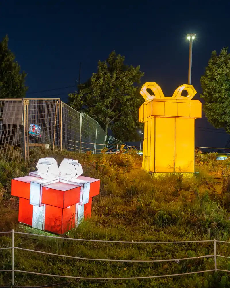 Paquets cadeaux géants lumineux, jaune et rouge, installés dans un parc la nuit