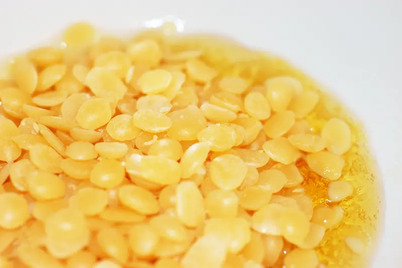 Yellow beeswax pellets slowly melting into a golden, glossy pool