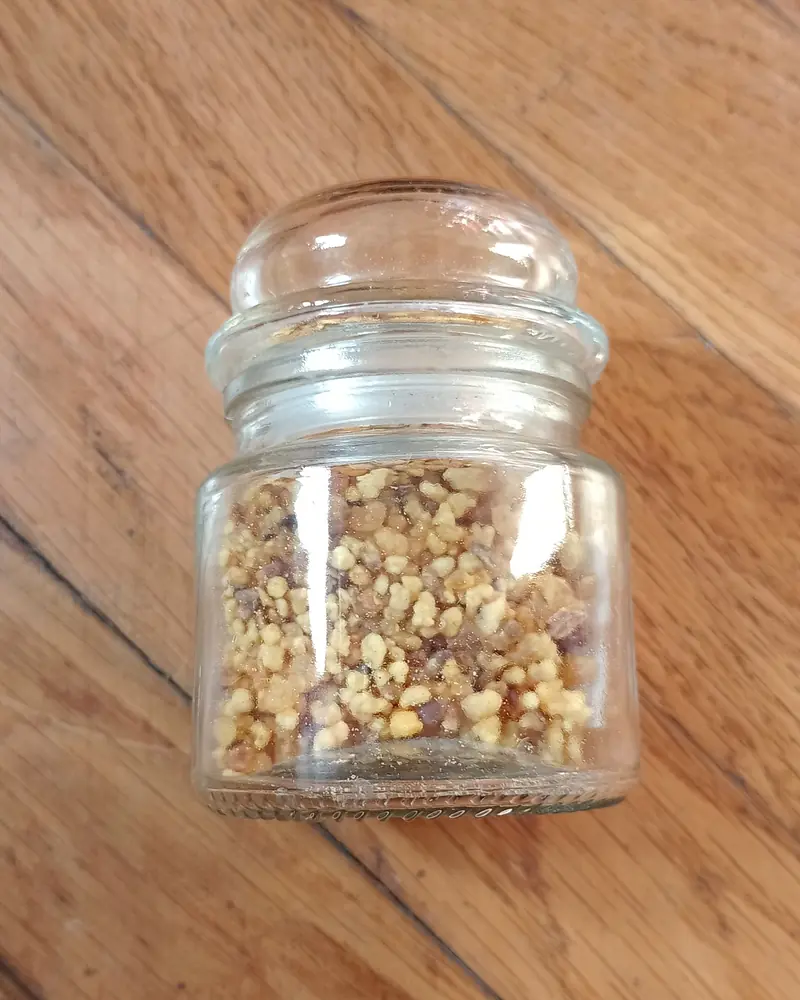 Small glass jar filled with golden frankincense grains on a wooden table