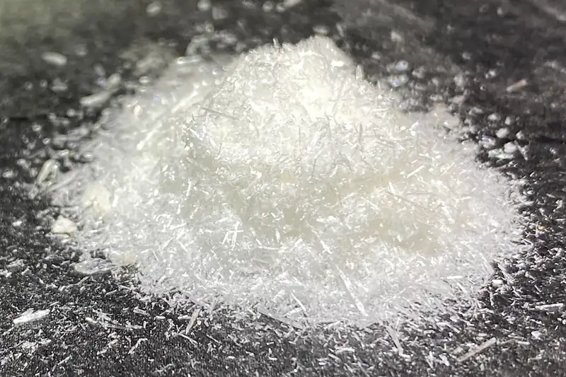 Petit tas de cristaux de vanilline blancs en aiguilles sur une surface sombre
