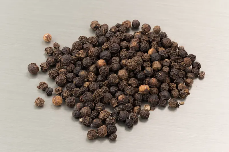Small heap of wrinkled black peppercorns on a pale background