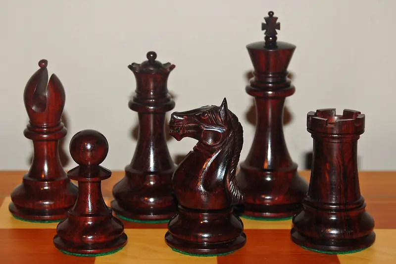 Dark red sandalwood chess pieces, king, queen, knight and rook, on a chessboard