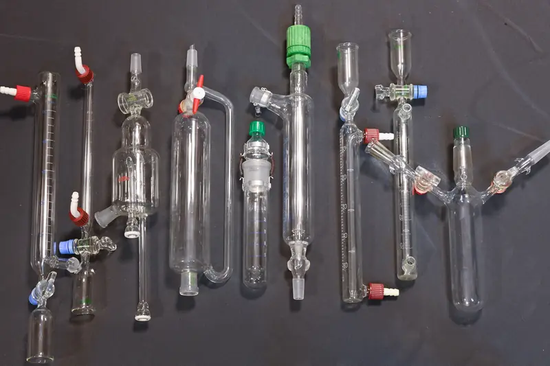 Pièces de verrerie de laboratoire alignées sur fond sombre, robinets verts et rouges