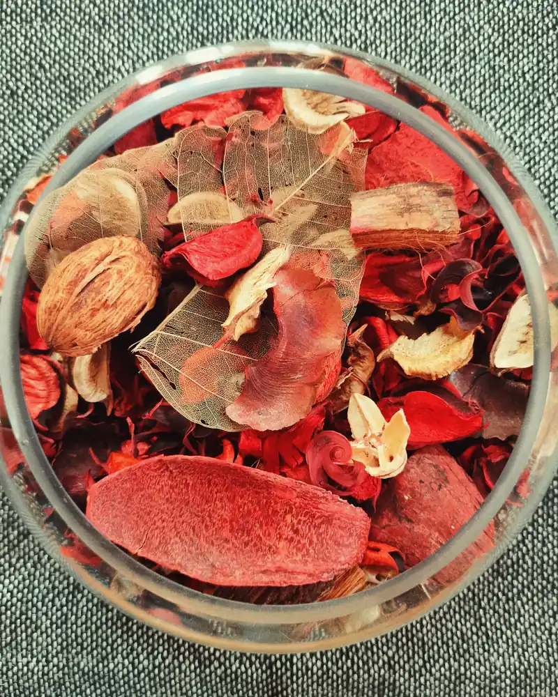 Potpourri of dried red and pink petals, barks and pods in a glass jar