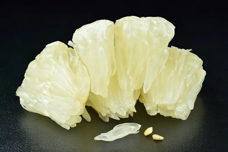 Peeled pomelo segments with translucent juice vesicles on black, with two seeds