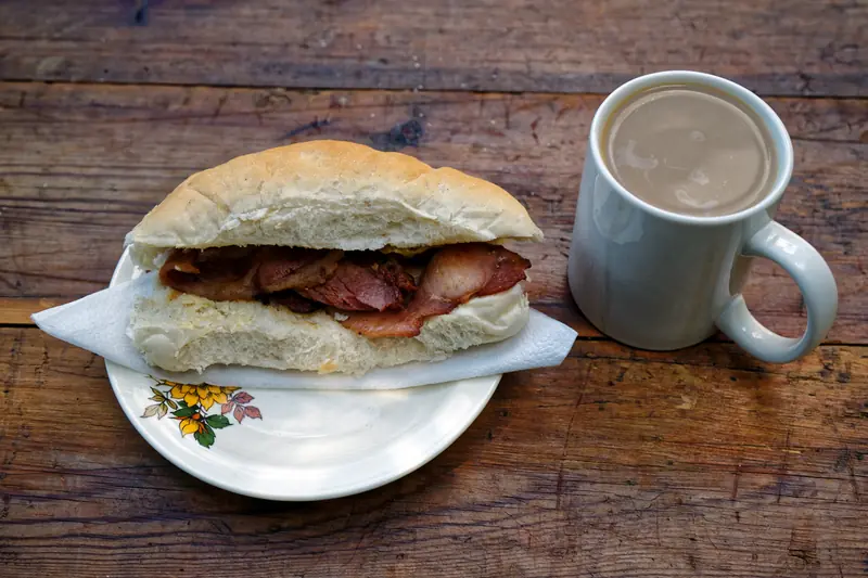 Bacon sandwich and a large mug of milky tea on a weathered wooden table